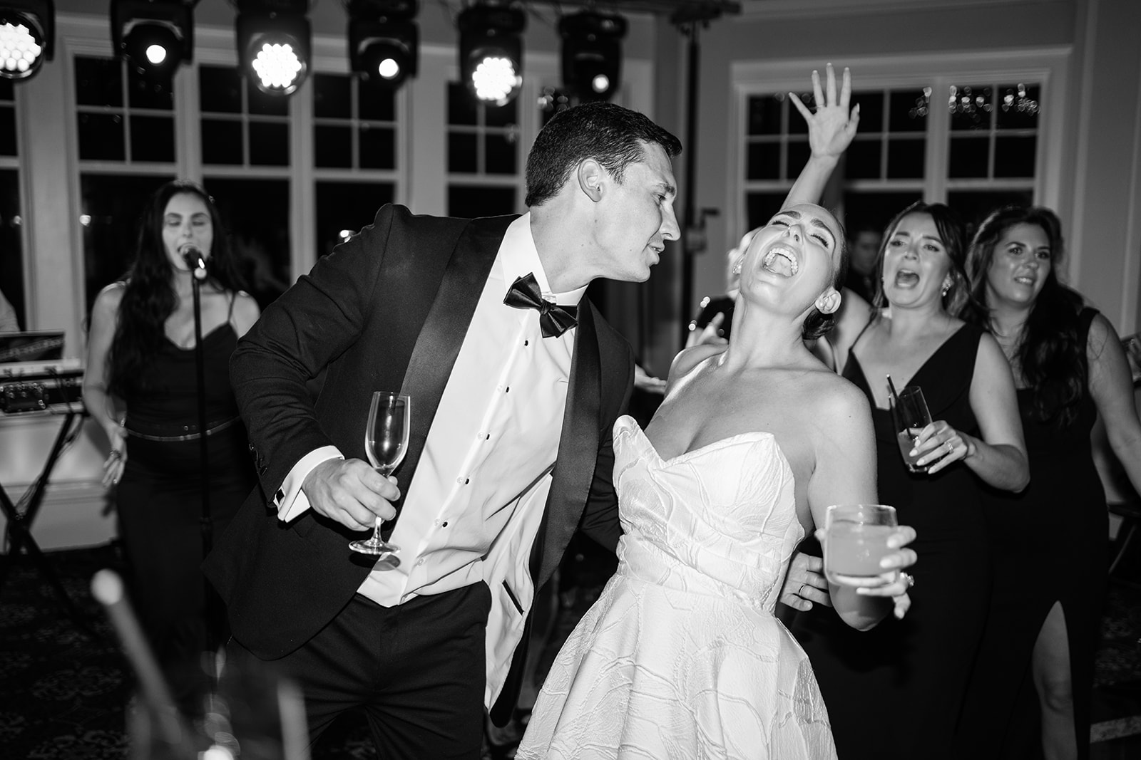 Black and white film photo of the bride and groom singing passionately on a crowded dance floor.